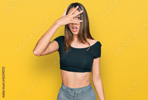 Young brunette woman wearing casual clothes peeking in shock covering face and eyes with hand, looking through fingers with embarrassed expression.