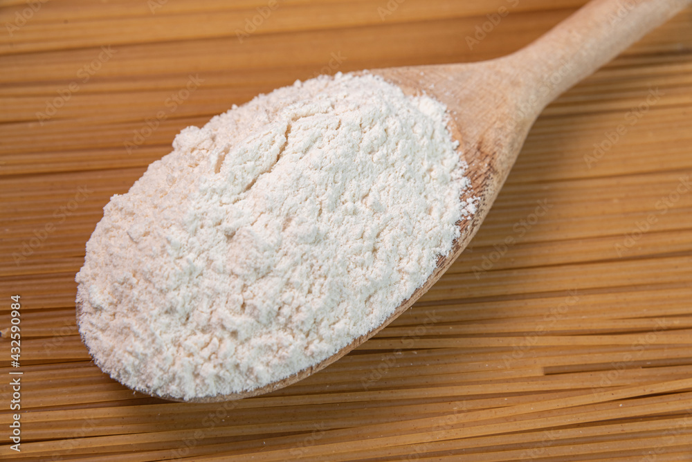 Wooden spoon with wheat flour over raw pasta Wooden spoon with wheat flour over raw pasta