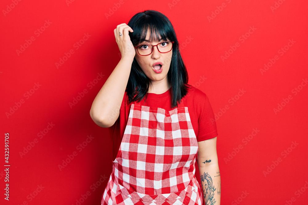 Young hispanic woman wearing cook apron and glasses surprised with hand on head for mistake, remember error. forgot, bad memory concept. Young hispanic woman wearing cook apron and glasses surprised with hand on head for mistake, remember error. forgot, bad memory concept.