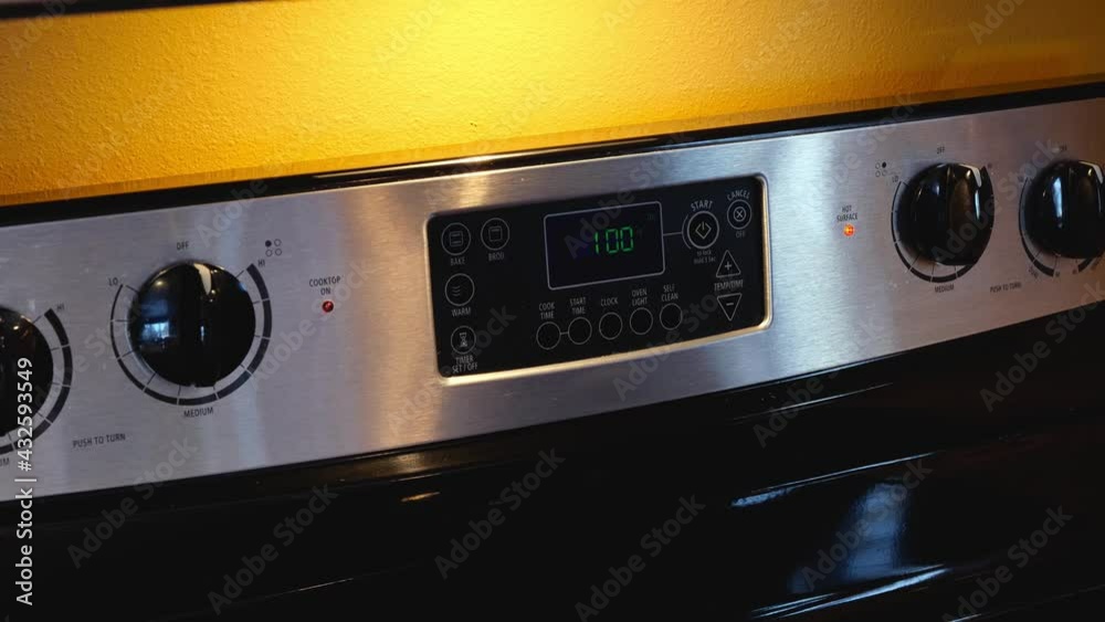 Womans hand regulating cooking on oven panel in kitchen. Woman setting temperature on control panel on modern electric oven appliance. Womans hand regulating cooking on oven panel in kitchen. Woman setting temperature on control panel on modern electric oven appliance.