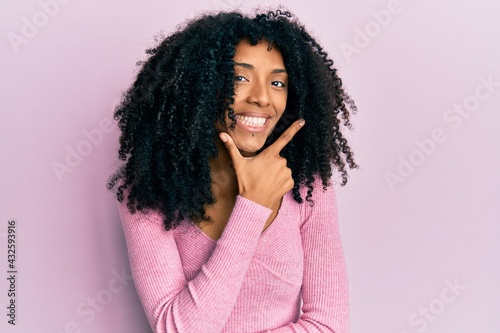 African american woman with afro hair wearing casual pink shirt looking confident at the camera smiling with crossed arms and hand raised on chin. thinking positive.