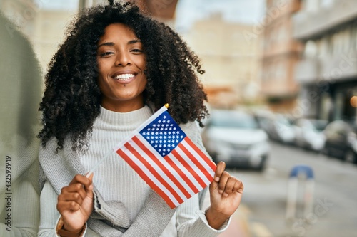 Young african american woman smiling happy holding United States flag at the city.