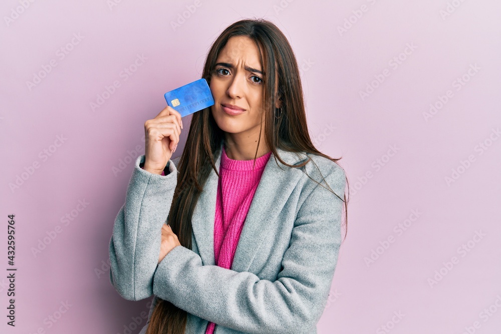 Young hispanic girl holding credit card in shock face, looking skeptical and sarcastic, surprised with open mouth Young hispanic girl holding credit card in shock face, looking skeptical and sarcastic, surprised with open mouth