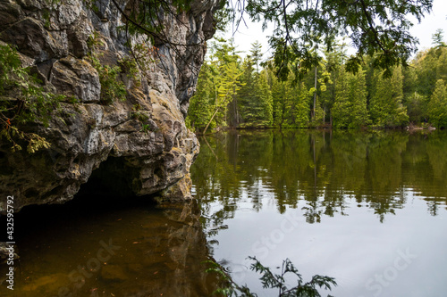A small cave at the side of a lake in Rockwood Conservation Area near Guelph, Ontario, with a forest in the background.