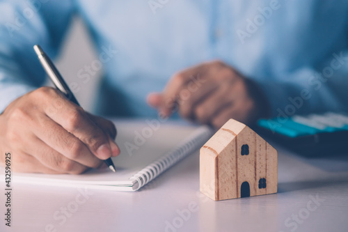 Hand of businessman planning and writing on note expense and mortgage with home, insurance house, finance and investment, calculate loan of residential, cost for refinance of property concept. photo