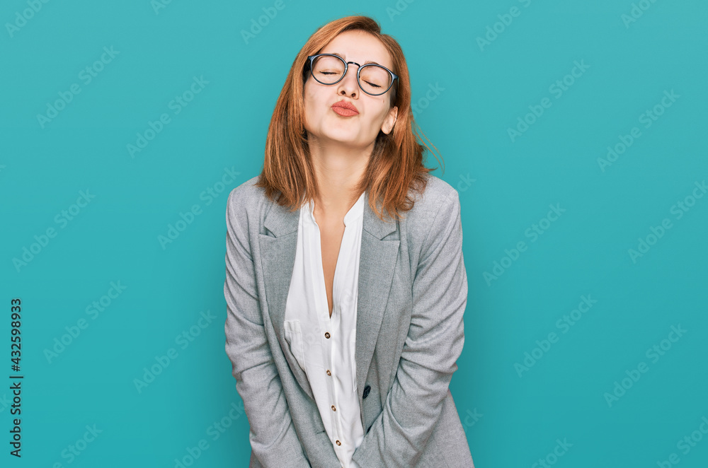 Young caucasian woman wearing business style and glasses looking at the camera blowing a kiss on air being lovely and sexy. love expression. Young caucasian woman wearing business style and glasses looking at the camera blowing a kiss on air being lovely and sexy. love expression.