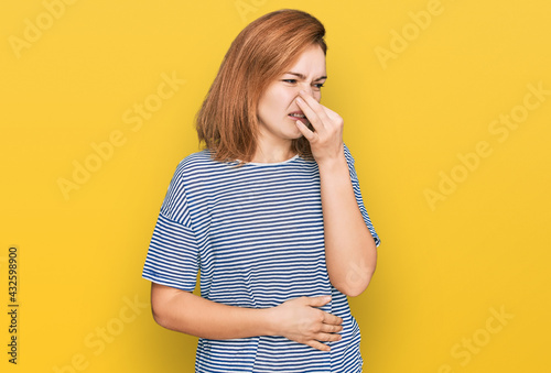 Young caucasian woman wearing casual clothes smelling something stinky and disgusting, intolerable smell, holding breath with fingers on nose. bad smell