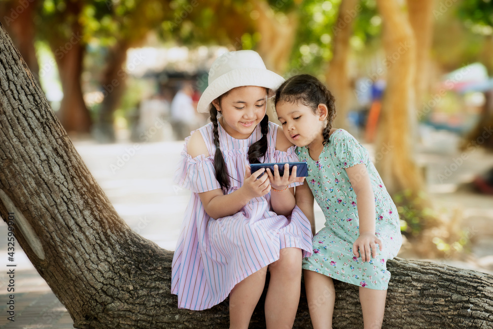 Obraz premium Cute two little kids girl using smartphone playing game in park