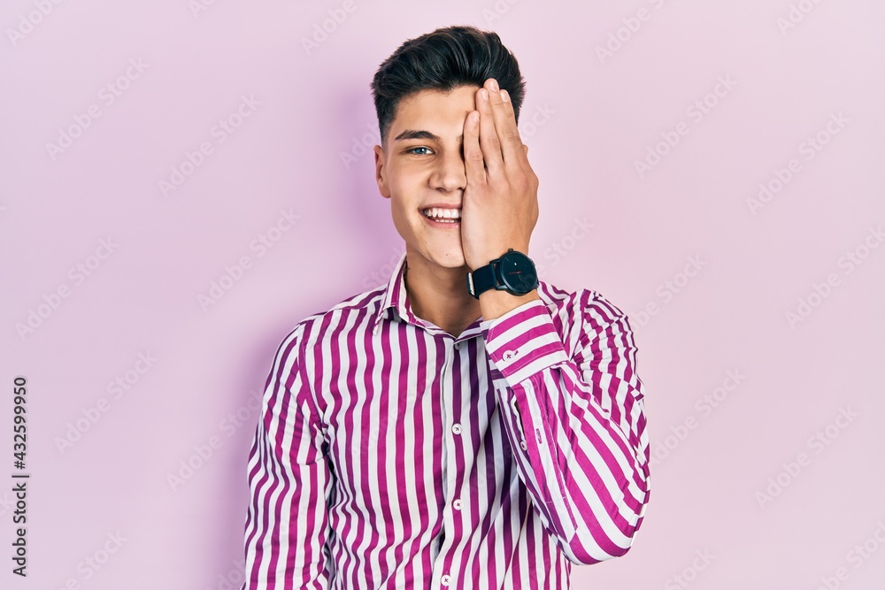 Young hispanic man wearing casual clothes covering one eye with hand, confident smile on face and surprise emotion. Young hispanic man wearing casual clothes covering one eye with hand, confident smile on face and surprise emotion.