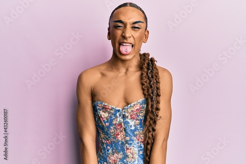 Hispanic man wearing make up and long hair wearing elegant corset sticking tongue out happy with funny expression. emotion concept.