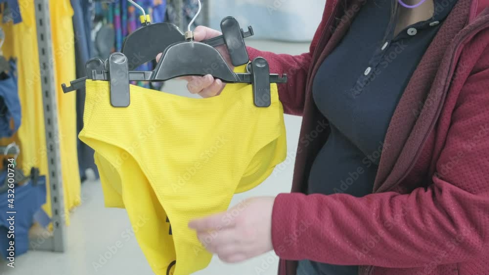 Caucasian pregnant woman chooses bright yellow, open swimsuit in store to buy. Concept of buying new clothes, fashion, beauty and an active lifestyle while carrying child. Hands close up shot Caucasian pregnant woman chooses bright yellow, open swimsuit in store to buy. Concept of buying new clothes, fashion, beauty and an active lifestyle while carrying child. Hands close up shot