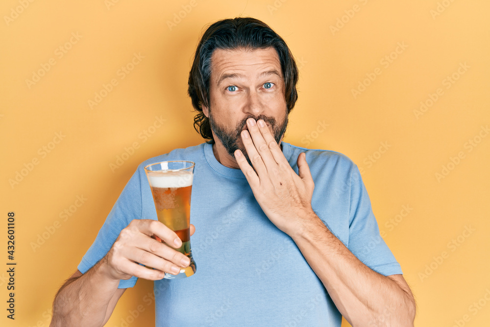 Middle age caucasian man drinking a pint of beer covering mouth with hand, shocked and afraid for mistake. surprised expression Middle age caucasian man drinking a pint of beer covering mouth with hand, shocked and afraid for mistake. surprised expression