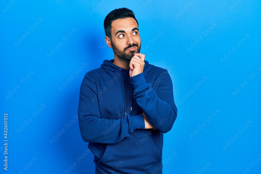 Handsome hispanic man with beard wearing casual sweatshirt thinking concentrated about doubt with finger on chin and looking up wondering Handsome hispanic man with beard wearing casual sweatshirt thinking concentrated about doubt with finger on chin and looking up wondering