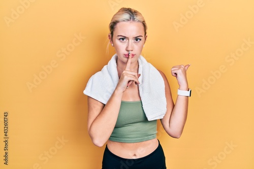 Young blonde girl wearing sportswear and towel asking to be quiet with finger on lips pointing with hand to the side. silence and secret concept. © Krakenimages.com