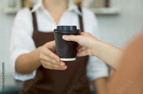 Young customer get hot coffee from the barista. Morning atmosphere in a coffee shop.