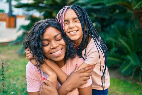 Beautiful african american mother and daughter smiling happy and hugging. Standing with smile on face standing at the park.