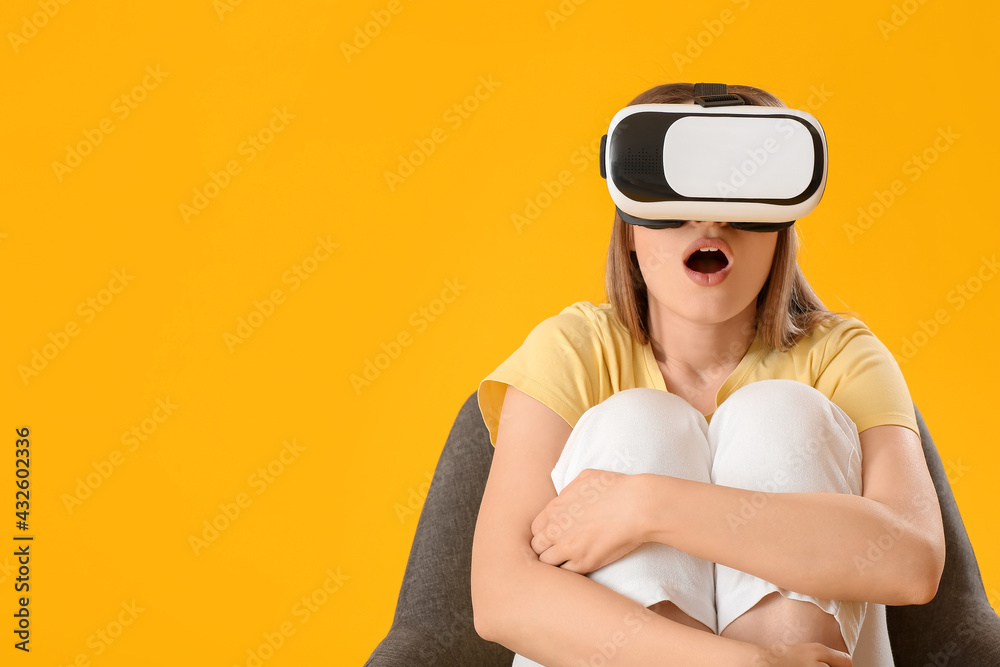 Surprised young woman with virtual reality glasses sitting in armchair on color background Surprised young woman with virtual reality glasses sitting in armchair on color background