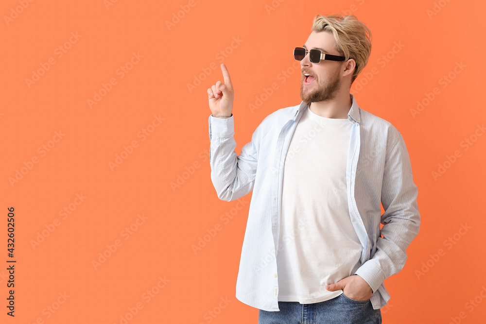 Young man with stylish sunglasses pointing at something on color background