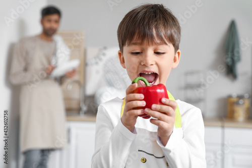 Cute little boy with healthy bell pepper in kitchen