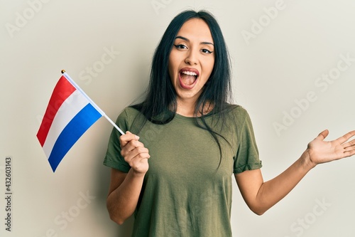 Young hispanic girl holding holland flag celebrating achievement with happy smile and winner expression with raised hand
