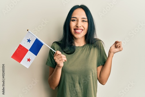 Young hispanic girl holding panama flag screaming proud, celebrating victory and success very excited with raised arm