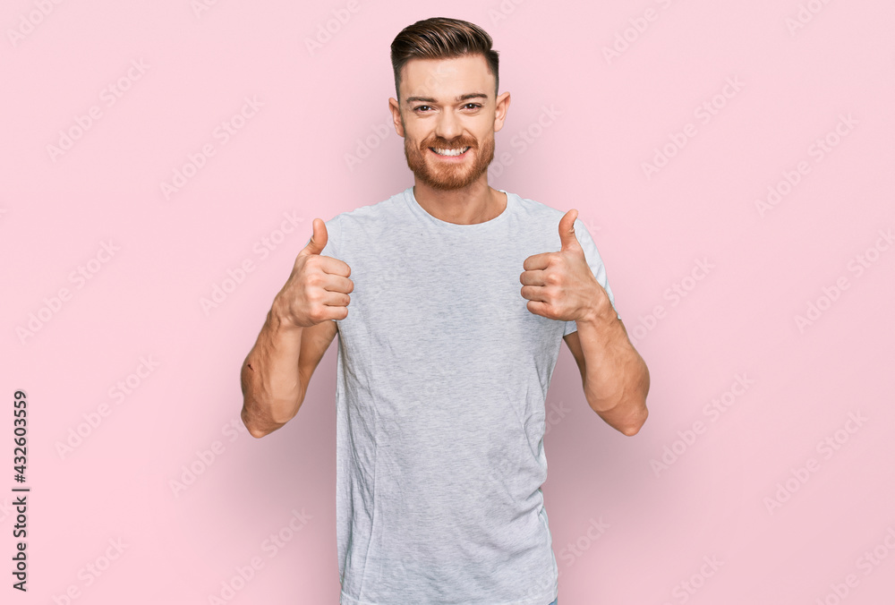 Young redhead man wearing casual grey t shirt success sign doing positive gesture with hand, thumbs up smiling and happy. cheerful expression and winner gesture. Young redhead man wearing casual grey t shirt success sign doing positive gesture with hand, thumbs up smiling and happy. cheerful expression and winner gesture.