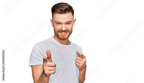 Young redhead man wearing casual grey t shirt pointing fingers to camera with happy and funny face. good energy and vibes.