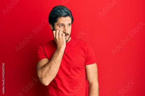 Young hispanic man wearing casual red t shirt looking stressed and nervous with hands on mouth biting nails. anxiety problem.