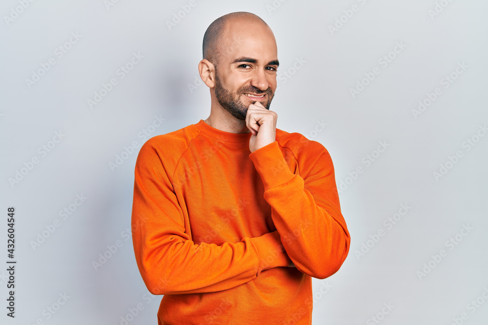 Young bald man wearing casual clothes smiling looking confident at the camera with crossed arms and hand on chin. thinking positive.