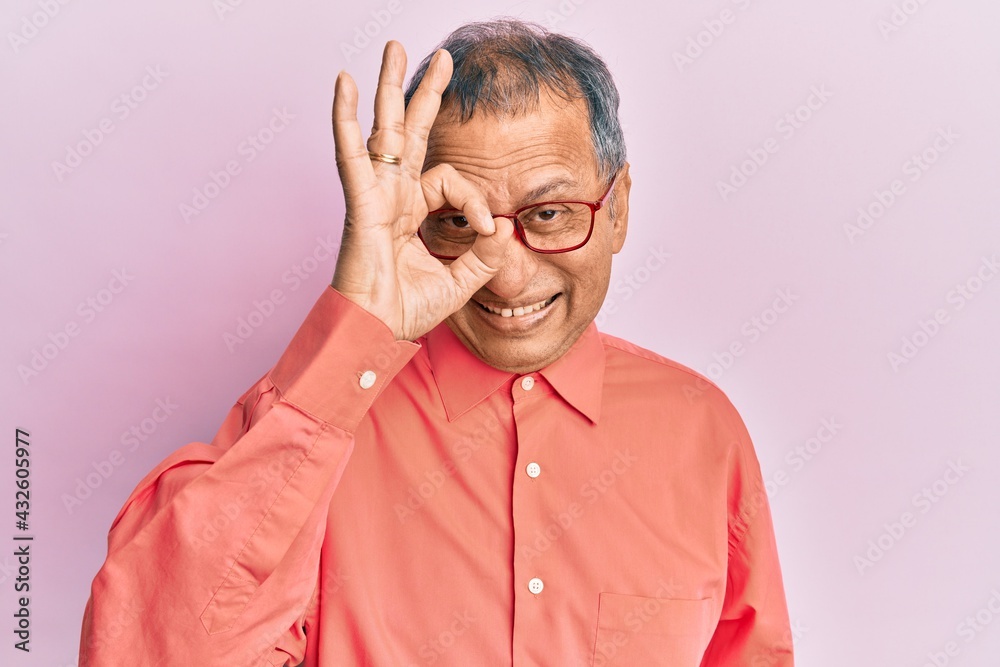 Middle age indian man wearing casual clothes and glasses doing ok gesture with hand smiling, eye looking through fingers with happy face.