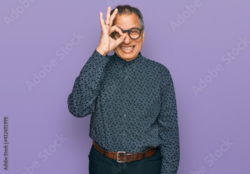 Middle age indian man wearing casual clothes and glasses doing ok gesture with hand smiling, eye looking through fingers with happy face.