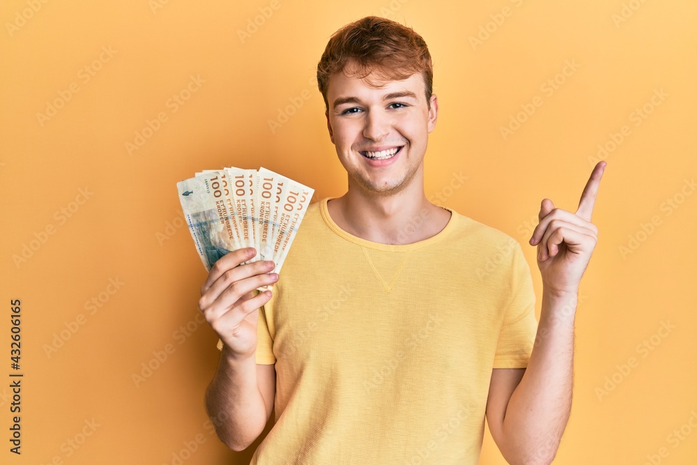 Young caucasian man holding 100 danish krone banknotes smiling happy pointing with hand and finger to the side Young caucasian man holding 100 danish krone banknotes smiling happy pointing with hand and finger to the side