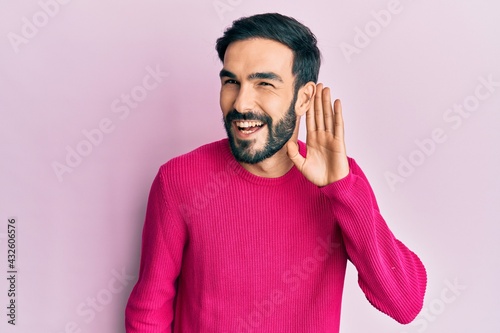 Young hispanic man wearing casual clothes smiling with hand over ear listening and hearing to rumor or gossip. deafness concept. © Krakenimages.com