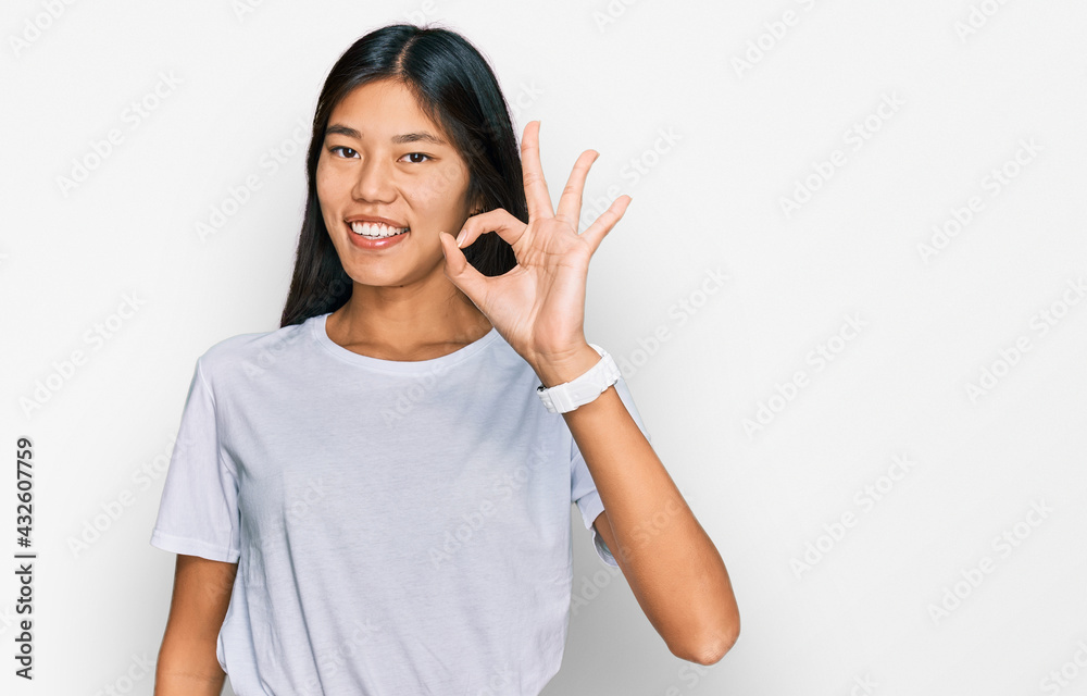 Beautiful young asian woman wearing casual white t shirt smiling positive doing ok sign with hand and fingers. successful expression. Beautiful young asian woman wearing casual white t shirt smiling positive doing ok sign with hand and fingers. successful expression.