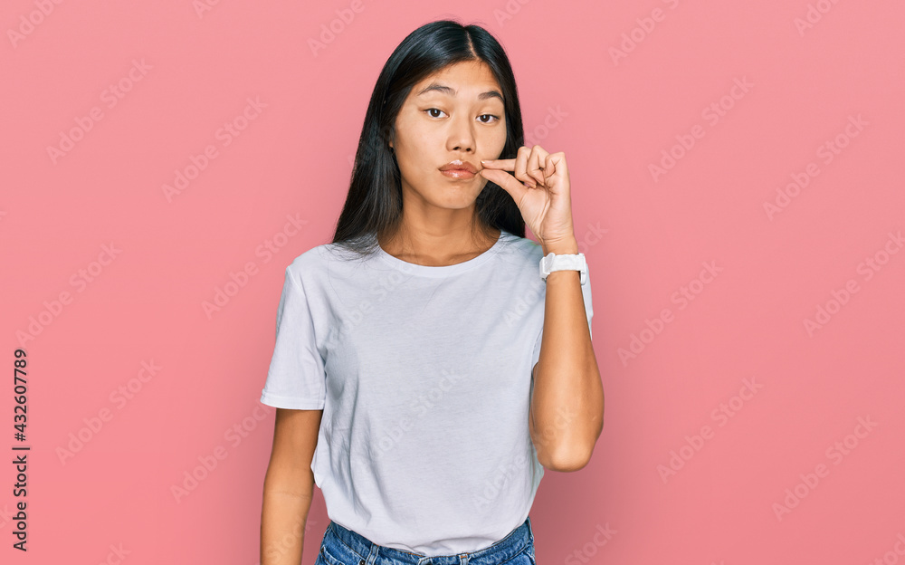 Fototapeta premium Beautiful young asian woman wearing casual white t shirt mouth and lips shut as zip with fingers. secret and silent, taboo talking
