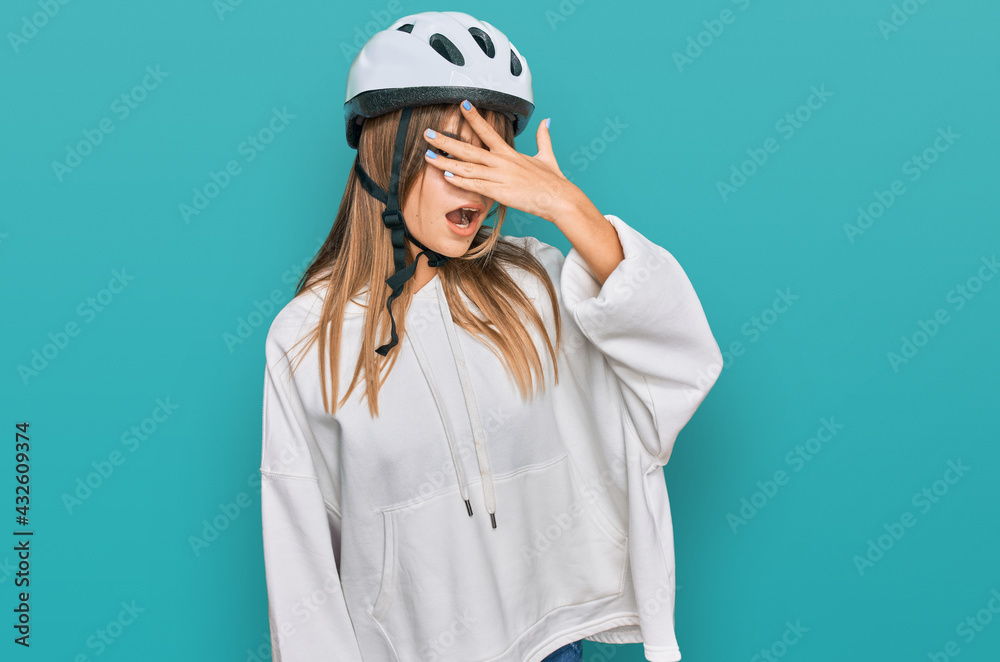 Teenager caucasian girl wearing bike helmet peeking in shock covering face and eyes with hand, looking through fingers with embarrassed expression. Teenager caucasian girl wearing bike helmet peeking in shock covering face and eyes with hand, looking through fingers with embarrassed expression.