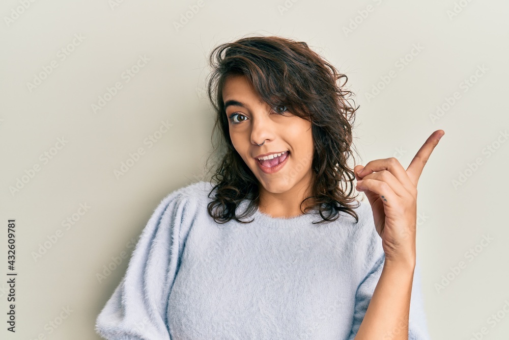 Young hispanic woman wearing casual winter sweater with a big smile on face, pointing with hand and finger to the side looking at the camera. Young hispanic woman wearing casual winter sweater with a big smile on face, pointing with hand and finger to the side looking at the camera.