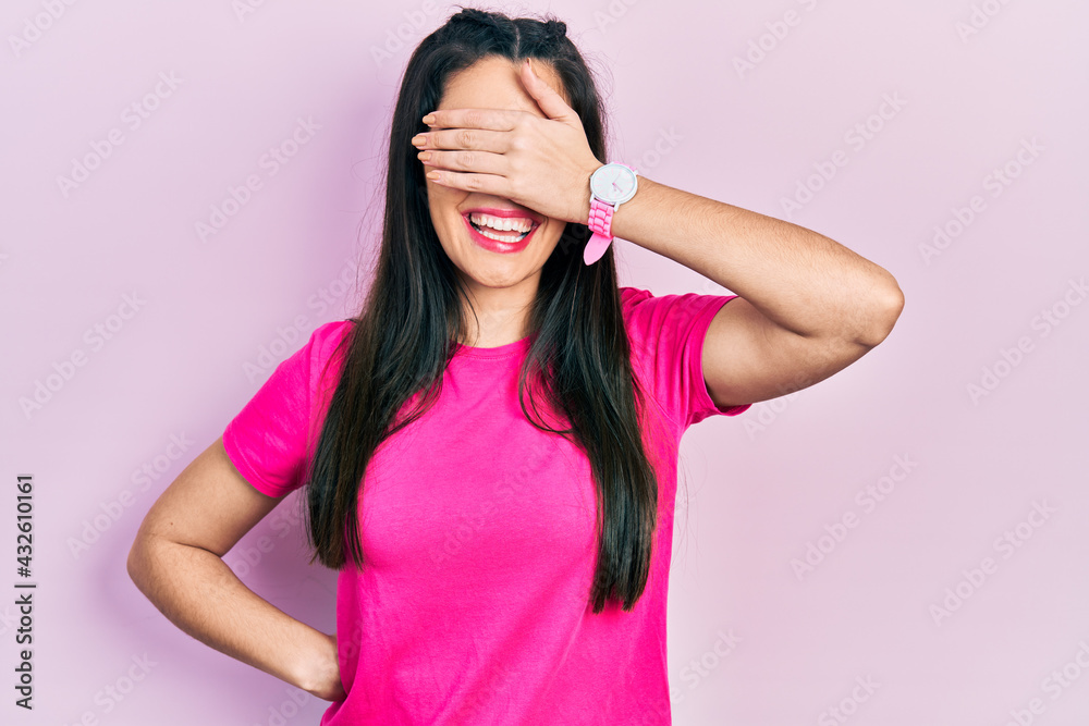 Young hispanic girl wearing casual pink t shirt smiling and laughing with hand on face covering eyes for surprise. blind concept. Young hispanic girl wearing casual pink t shirt smiling and laughing with hand on face covering eyes for surprise. blind concept.