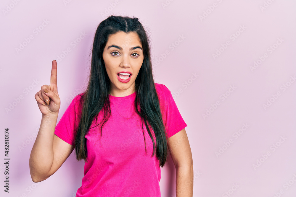 Young hispanic girl wearing casual pink t shirt pointing finger up with successful idea. exited and happy. number one. Young hispanic girl wearing casual pink t shirt pointing finger up with successful idea. exited and happy. number one.