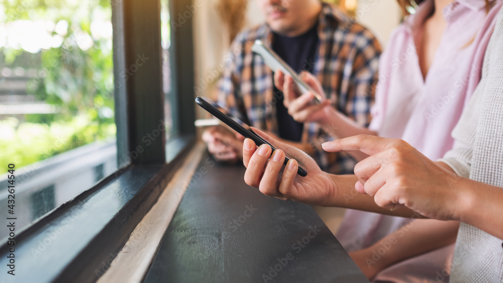 Obraz premium Group of young people holding and using their mobile phones while sitting together