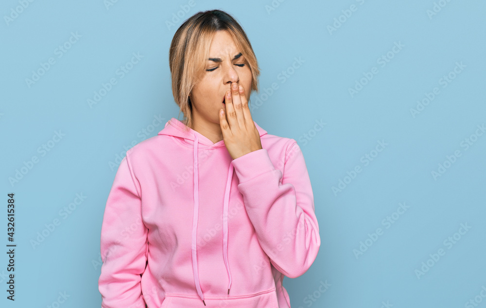 Young caucasian woman wearing casual sweatshirt bored yawning tired covering mouth with hand. restless and sleepiness. Young caucasian woman wearing casual sweatshirt bored yawning tired covering mouth with hand. restless and sleepiness.