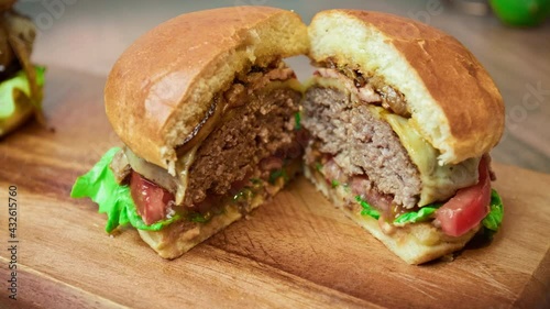 Close-up beef burger being sliced in half on the table in 4K. Serving burger from beef steak mince, sauce, bun, caramelised onions, cheese, tomato, lettuce.