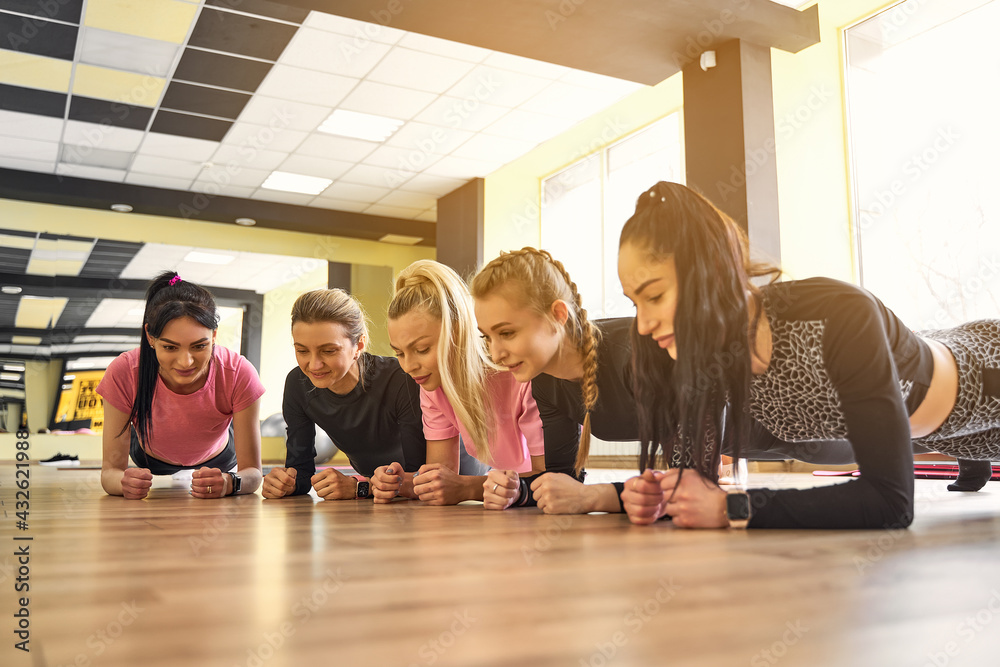 Group of young women doing plank together in gym