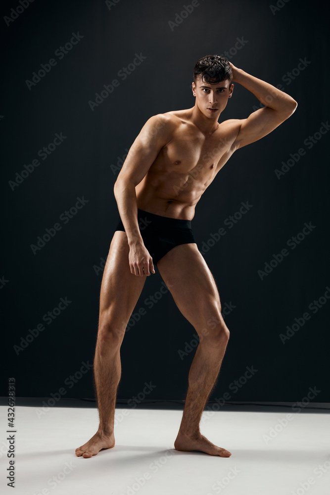 Naklejka premium sporty man with muscular naked body in black panties on a dark background