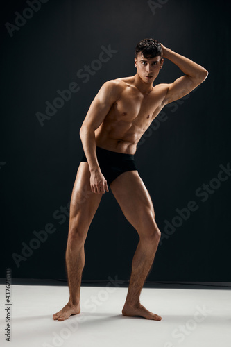 sporty man with muscular naked body in black panties on a dark background