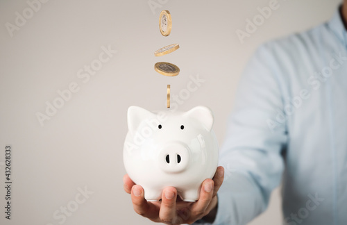 Fotografija Businessman holding white piggy with coins falling for money saving and deposit concept
