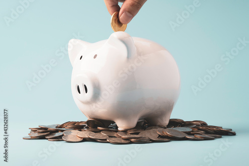 Hand putting coin to white piggy saving on coins stacking , Financial money and bank deposit for investment concept.