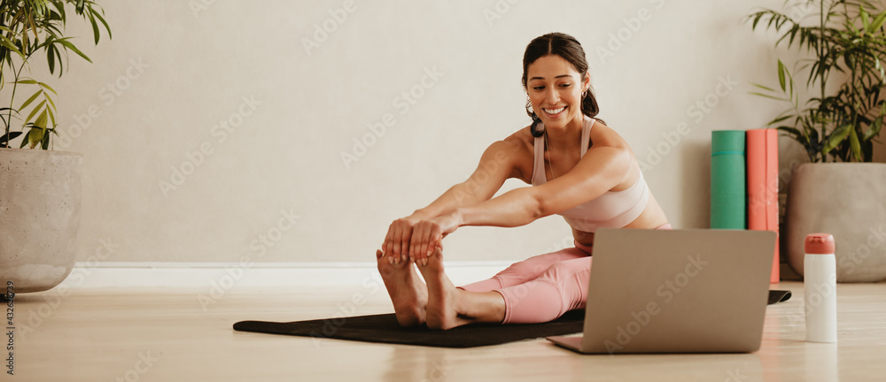 Woman doing yoga watching video on laptop - obrazy, fototapety, plakaty 