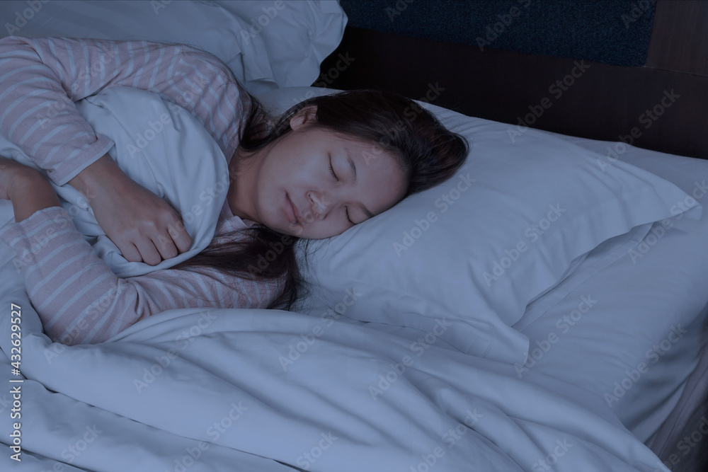 An Asian Woman who has dark brown hair wearing long sleeve t-shirt is sleeping on the bed. in darkness room. An Asian Woman who has dark brown hair wearing long sleeve t-shirt is sleeping on the bed. in darkness room.