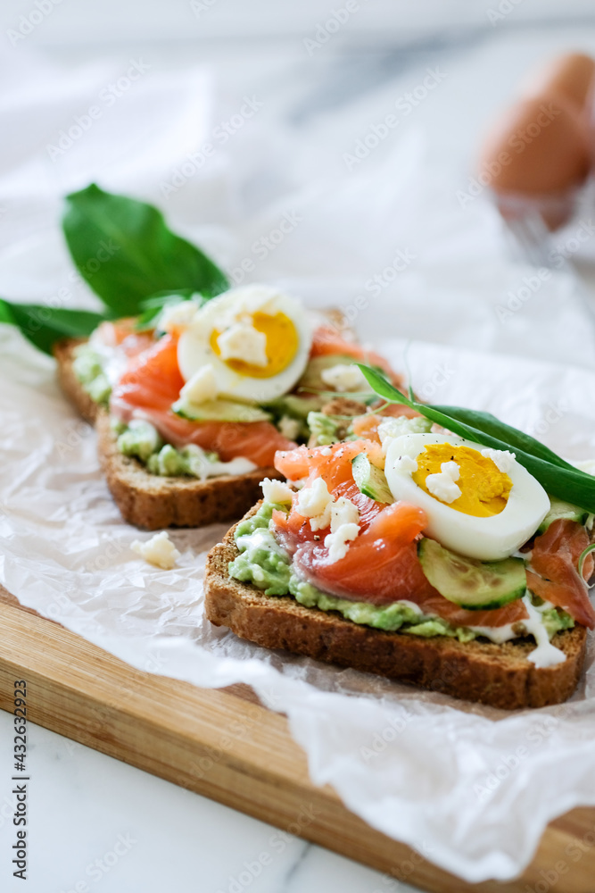 Open sandwich traditional danish smorrebrod salmon, cucumber, boiled egg, soft cheese. Homemade sandwich with rye bread on white background, top view. Tasty salmon fish sandwich closeup Open sandwich traditional danish smorrebrod salmon, cucumber, boiled egg, soft cheese. Homemade sandwich with rye bread on white background, top view. Tasty salmon fish sandwich closeup
